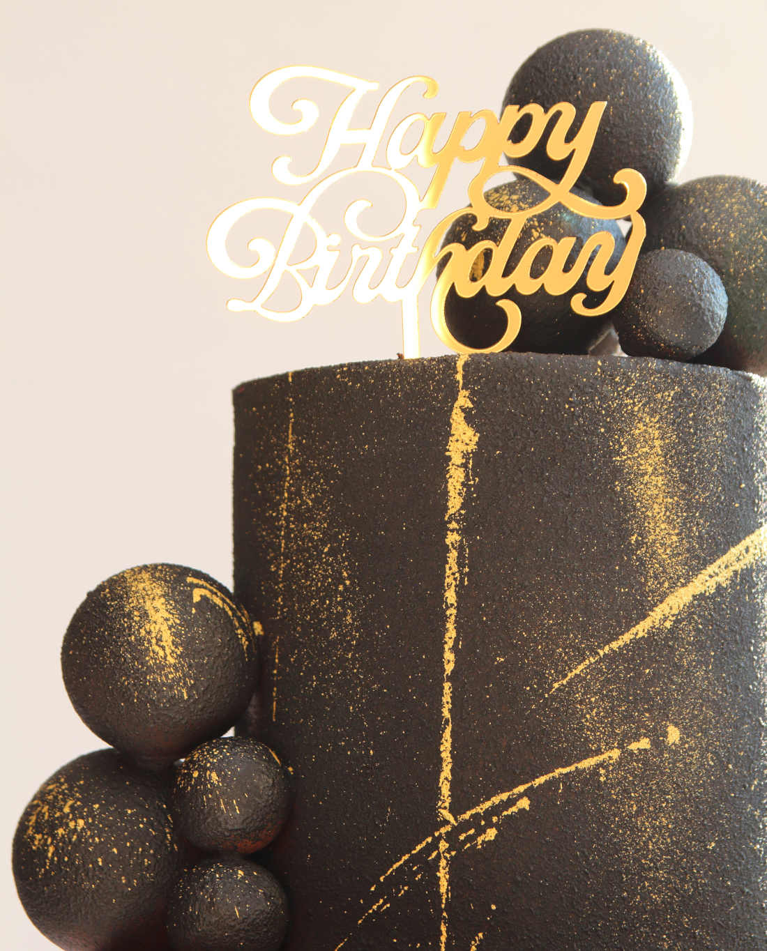 Gold decorations and spheres on a black birthday cake